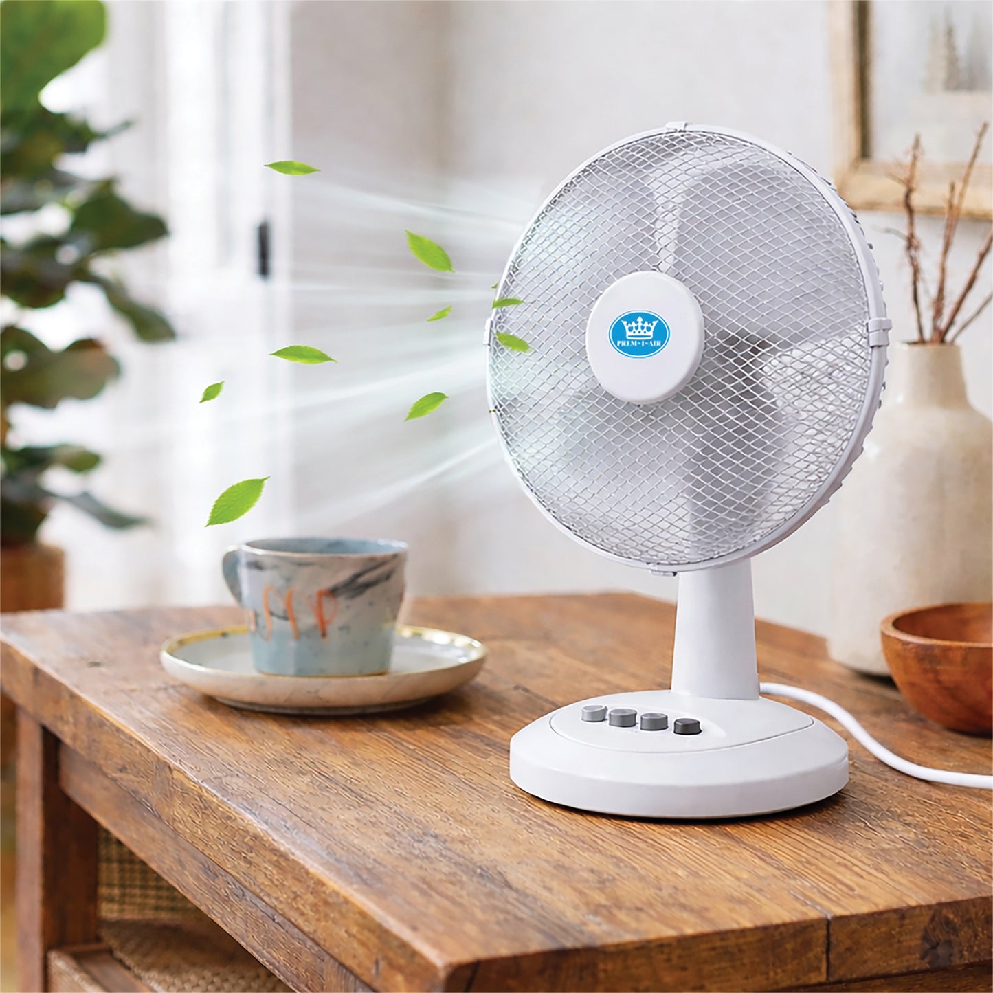 White desk fan on a wooden table with a cup and plant in the background